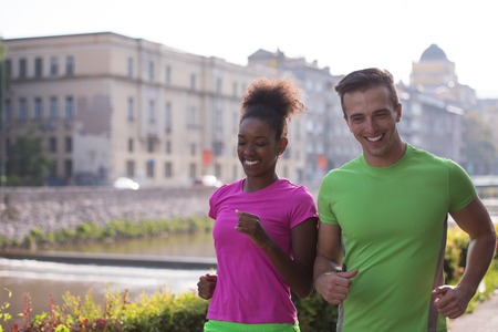 healthy young multiethnic couple jogging in the city at early morning with sunrise in backgroundの写真素材