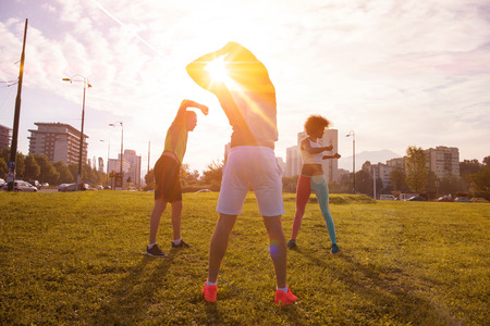 multiethnic group of young people stretching before running with the sunrise in the cityの写真素材