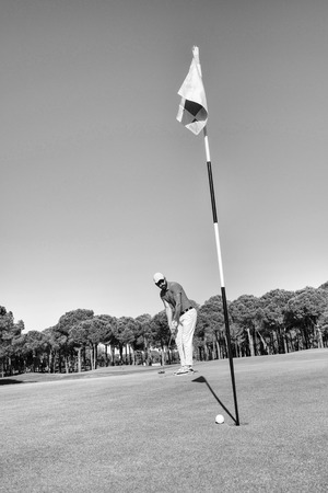 golf player hitting shot with club on course at beautiful morning with sun flare in background black and whiteの写真素材