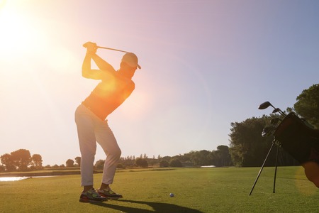 golf player hitting shot with club on course at beautiful morning with sun flare in backgroundの写真素材
