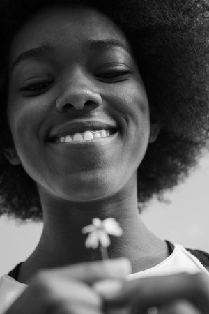 portrait of a young beautiful African American girl with a flower of daisy in her handの写真素材