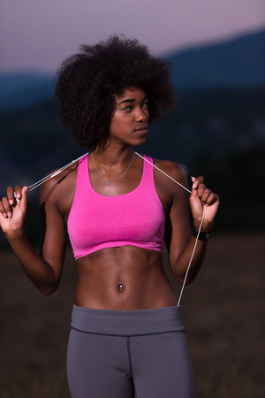 portrait of a young beautiful african american woman with headphones jogging in nature beautiful summer nightの写真素材