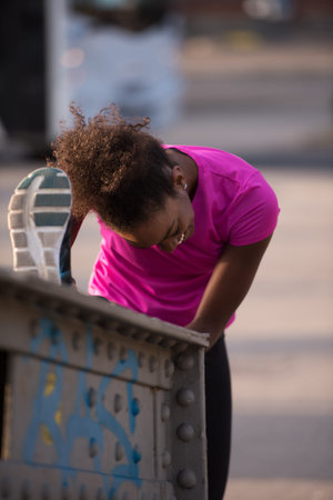 young beautiful African American woman doing warming up and stretching with her leg raised to the...