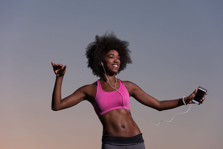 Young beautiful black girl laughs and dances outdoors with a mobile phone in her hands in a meadow...