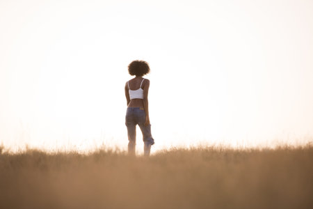 Young beautiful black girl laughs and dances outdoors in a meadow during sunset