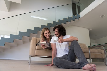 Young couple relaxing at luxurious home with tablet computers reading in the living room on the sofa couch.の写真素材