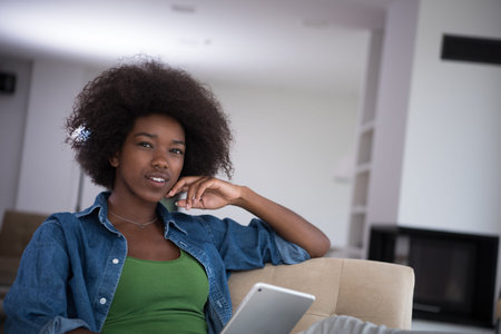 Young african american woman at home relaxing in her luxury lliving room reading a digital tablet PC surf internet and workの写真素材
