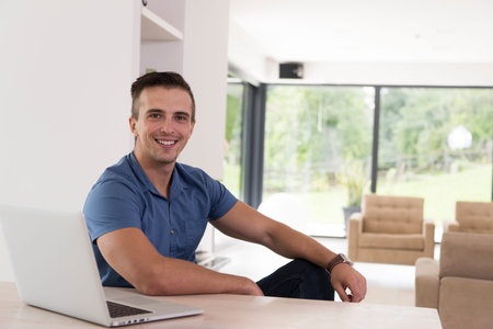 Young man with his laptop computer at his luxury modern home, smilingの写真素材