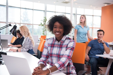 young smiling African American informal businesswoman working in the office with colleagues in the backgroundの写真素材