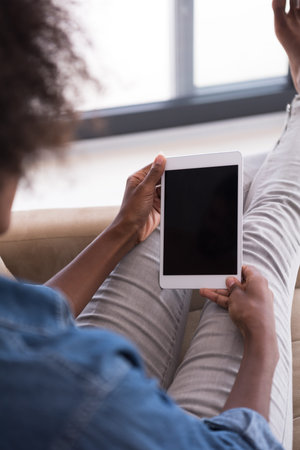 Young african american woman at home relaxing in her luxury lliving room reading a digital tablet PC...