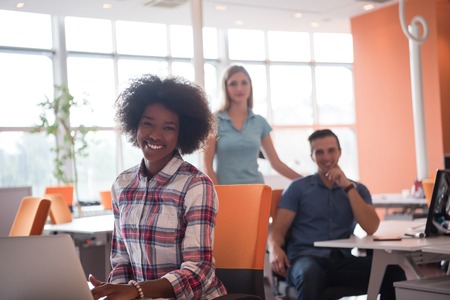 young smiling African American informal businesswoman working in the office with colleagues in the backgroundの写真素材