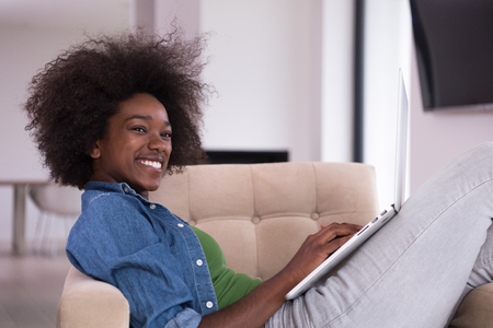 Young african american woman at home in the chair relaxing in her luxury lliving room reading  laptop PC surf internet and workの写真素材