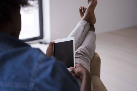 Young african american woman at home relaxing in her luxury lliving room reading a digital tablet PC surf internet and workの写真素材