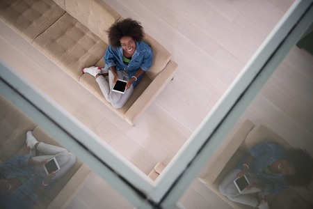 Young african american woman at home relaxing in her luxury lliving room reading a digital tablet PC surf internet and work top viewの写真素材