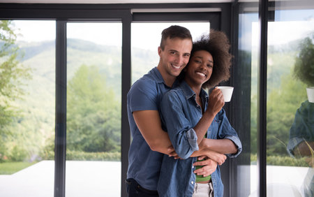 romantic happy young multiethnic couple enjoying morning coffee by the window in their luxury homeの写真素材