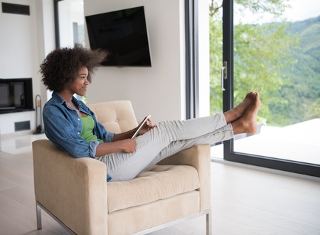 Young african american woman at home relaxing in her luxury lliving room reading a digital tablet PC surf internet and workの写真素材