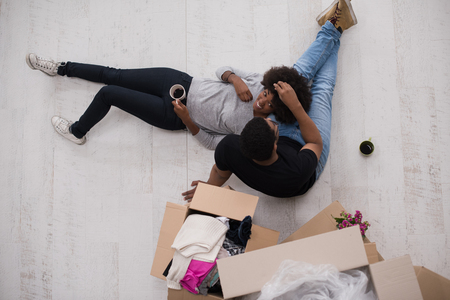 Relaxing in new house. Cheerful young African American couple sitting on the floor and drinking coffee while cardboard boxes laying all around themの写真素材
