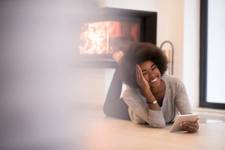 beautiful young black women used tablet computer on the floor of her luxury home in front of fireplace autumn dayの写真素材