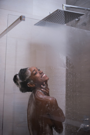 Woman in the shower,beautiful black young female showering under refreshing water, healthy lifestyle, enjoying time in luxury spa resortの写真素材