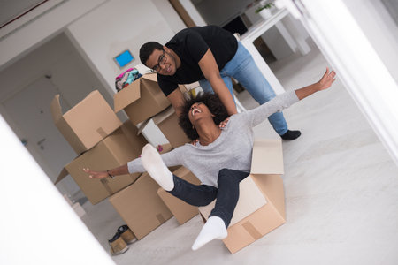 African American couple sitting in a box playing with packing material, having fun after moving in new homeの写真素材