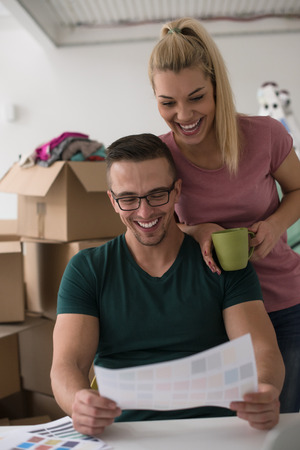 Young couple moving in a new home. Man and woman at the table using notebook laptop computer and plans with boxes around themの写真素材