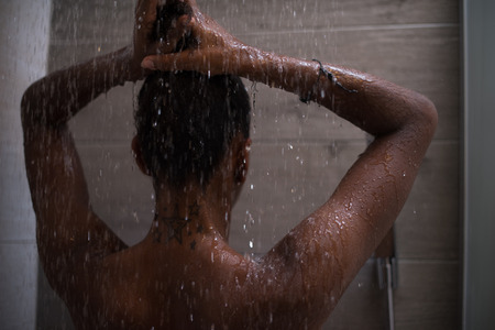 Woman in the shower,beautiful black young female showering under refreshing water, healthy lifestyle, enjoying time in luxury spa resortの写真素材