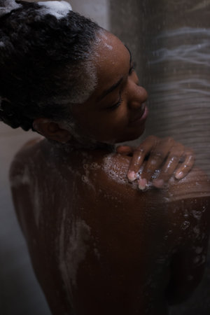 Woman in the shower,beautiful black young female showering under refreshing water, healthy lifestyle, enjoying time in luxury spa resortの写真素材