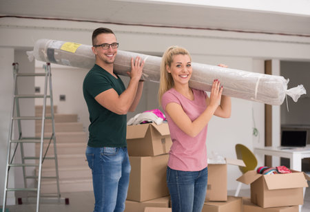 Young couple carrying a carpet moving in to new home together. Home, people, moving and real estate conceptの写真素材