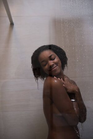 Woman in the shower,beautiful black young female showering under refreshing water, healthy lifestyle, enjoying time in luxury spa resortの写真素材