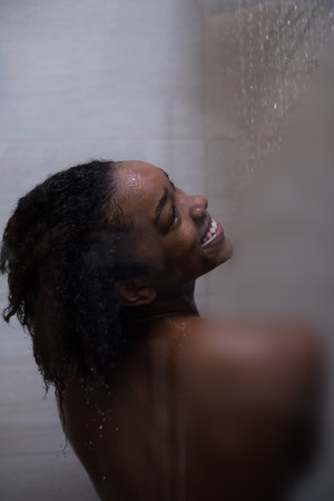 Woman in the shower,beautiful black young female showering under refreshing water, healthy lifestyle, enjoying time in luxury spa resortの写真素材
