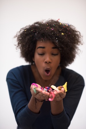 beautiful young black woman celebrating new year and chrismas party while blowing confetti decorations to cameraの写真素材