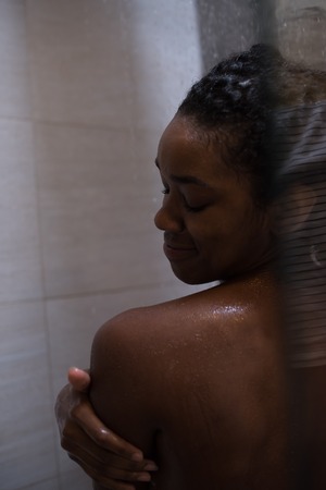 Woman in the shower,beautiful black young female showering under refreshing water, healthy lifestyle, enjoying time in luxury spa resortの写真素材