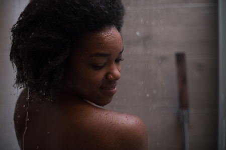 Woman in the shower,beautiful black young female showering under refreshing water, healthy lifestyle, enjoying time in luxury spa resortの写真素材