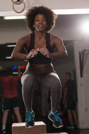 Fit young african american woman box jumping at a crossfit style gym. Female athlete is performing...