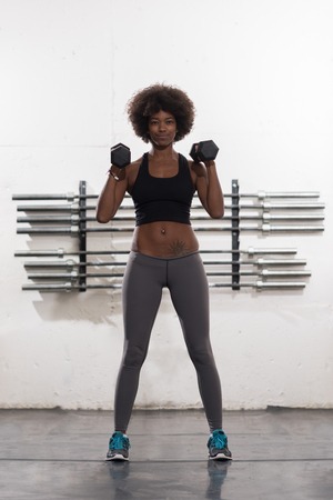 young beautiful African American woman doing bicep curls in a gymの写真素材