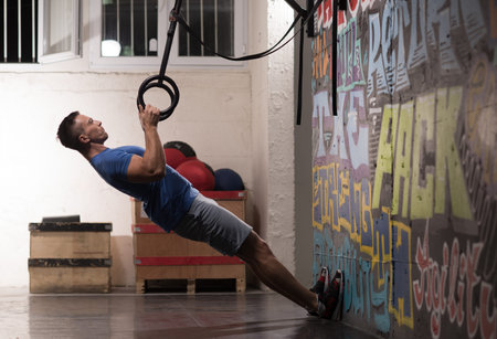 Fitness handsome man doing dipping exercise using rings in the gym