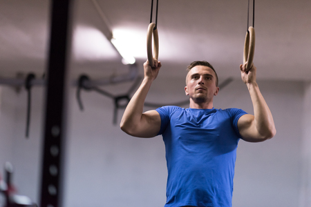 Fitness handsome man doing dipping exercise using rings in the gymの写真素材