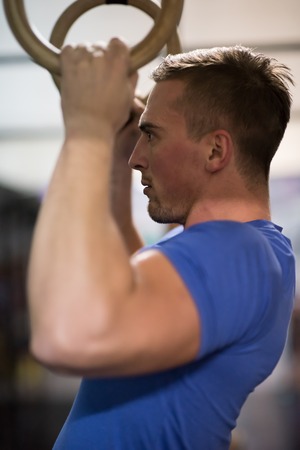 Fitness handsome man doing dipping exercise using rings in the gymの写真素材