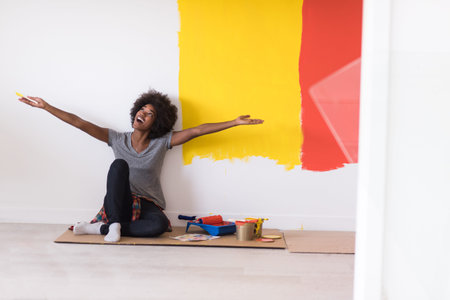 Portrait of a beautiful african american female painter sitting on floor near wall after painting.の写真素材