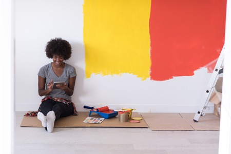 Portrait of a beautiful african american female painter sitting on floor near wall after painting.の写真素材