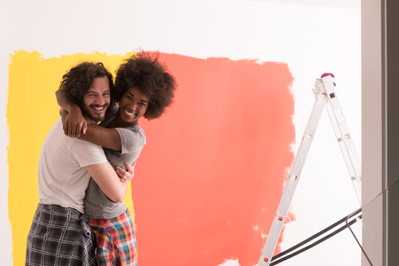 Young happy multiethnic couple hugging while they painting a wall in their new homeの写真素材