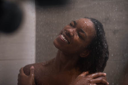 Woman in the shower,beautiful black young female showering under refreshing water, healthy lifestyle, enjoying time in luxury spa resortの写真素材