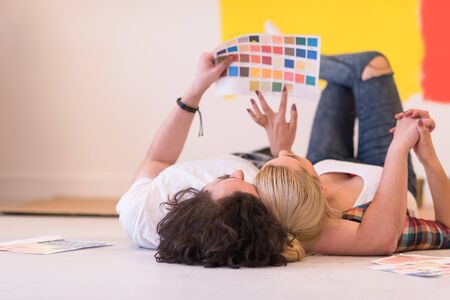 Happy young couple relaxing after painting a room in their new house on the floorの写真素材