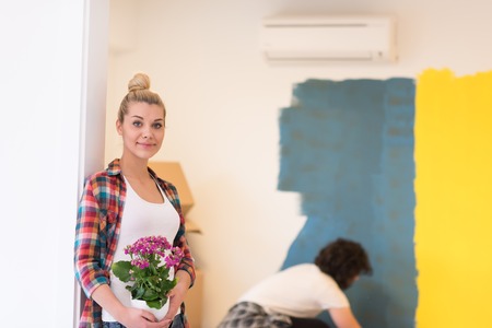 Happy couple doing home renovations, the man is painting the room and the woman hold the pot with flowersの写真素材