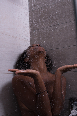 Woman in the shower,beautiful black young female showering under refreshing water, healthy lifestyle, enjoying time in luxury spa resortの写真素材
