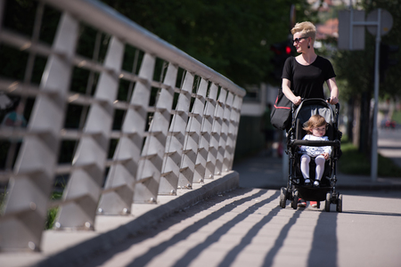 beautiful young mother with blond hair and sunglasses pushed her baby daughter in a stroller on a summer dayの写真素材