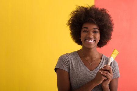 portrait of a young beautiful African American woman painting wall in her new apartmentの写真素材
