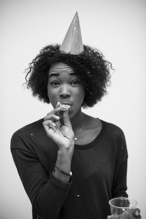 portrait of a young beautiful black woman in party hat blowing in whistle isolated on a white backgroundの写真素材