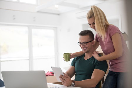 Young couple moving in a new home. Man and woman at the table using notebook laptop computer and plans with boxes around themの写真素材