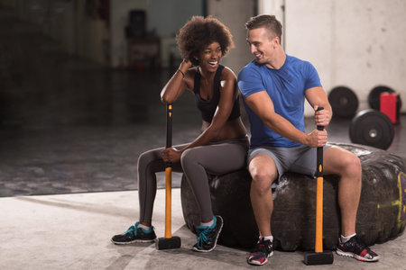 portrait of a young multiethnic couple after training with a sledgehammer and tractor tireの写真素材